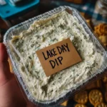 A creamy bowl of Lake Day Dip made with sour cream, ranch seasoning, green chiles, and shredded cheese, served with tortilla chips on a bright summer snack table.